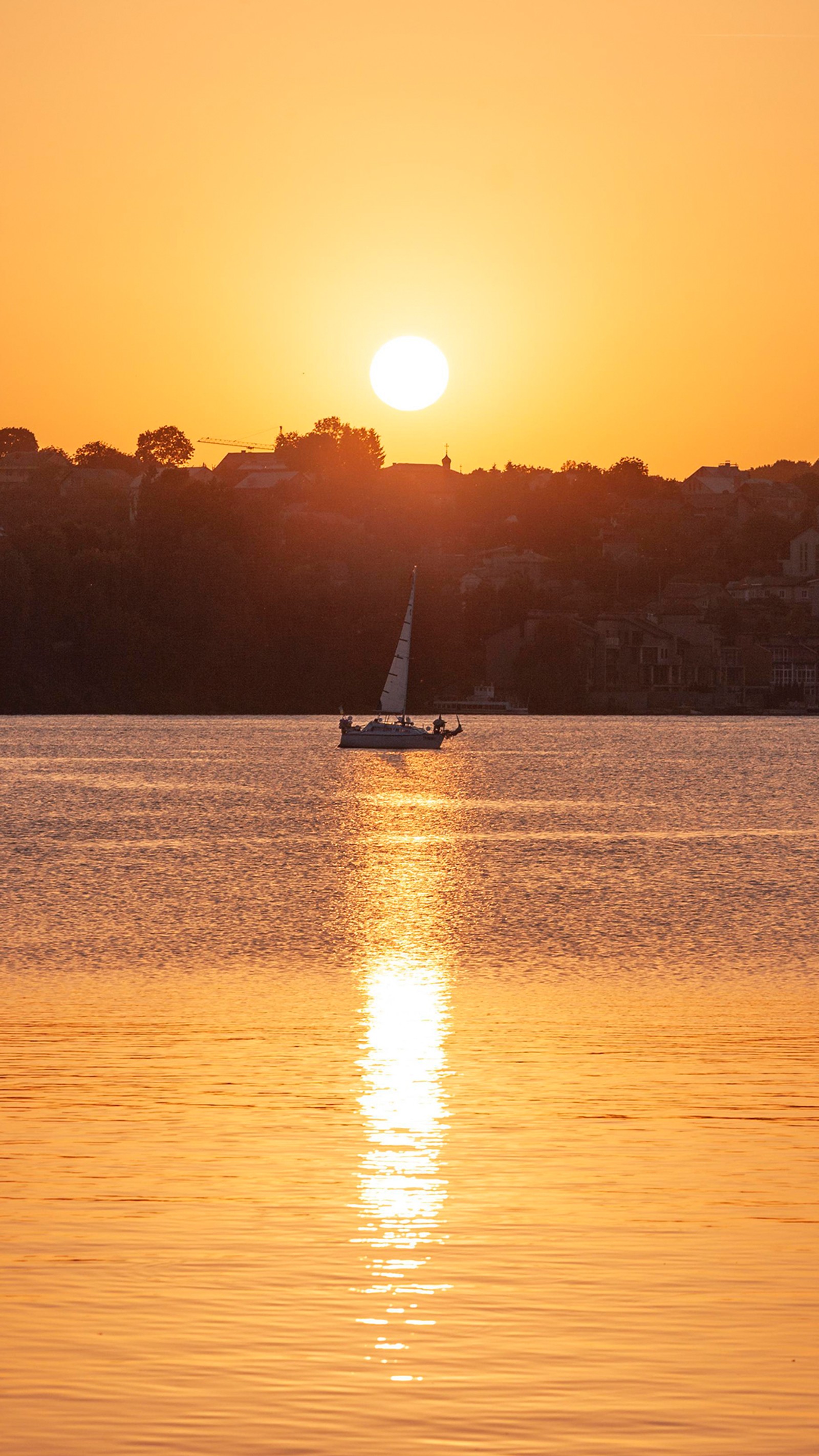 Arafed sailboat in the water at sunset with a city in the background (horizon, ship, water, boat, atmosphere)