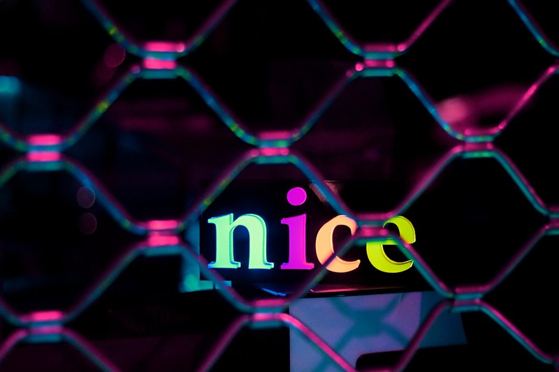 Неоновая вывеска со словом 'nice' за цепной забор (фиолетовый, свет, неон, розовый, освещение спецэффектов)