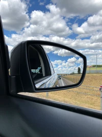 Reflexiones de un viaje: el espejo lateral de un coche compacto contra un cielo nublado