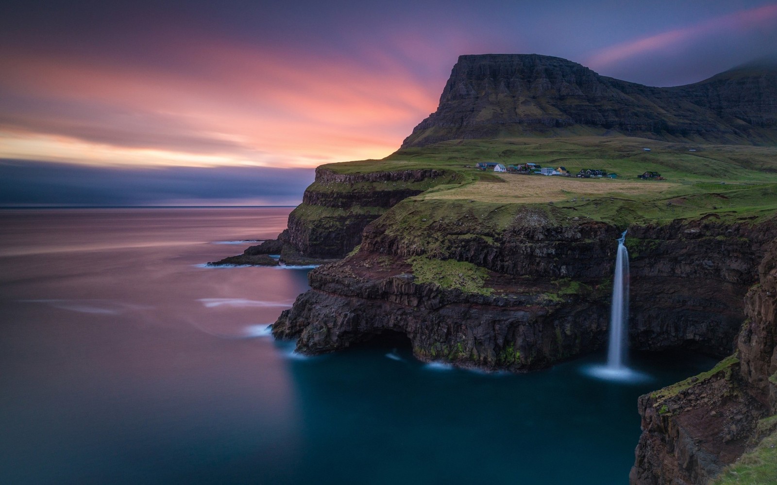 A waterfall flowing into the ocean at sunset near a mountain (waterfall, nature, sea, coast, headland)