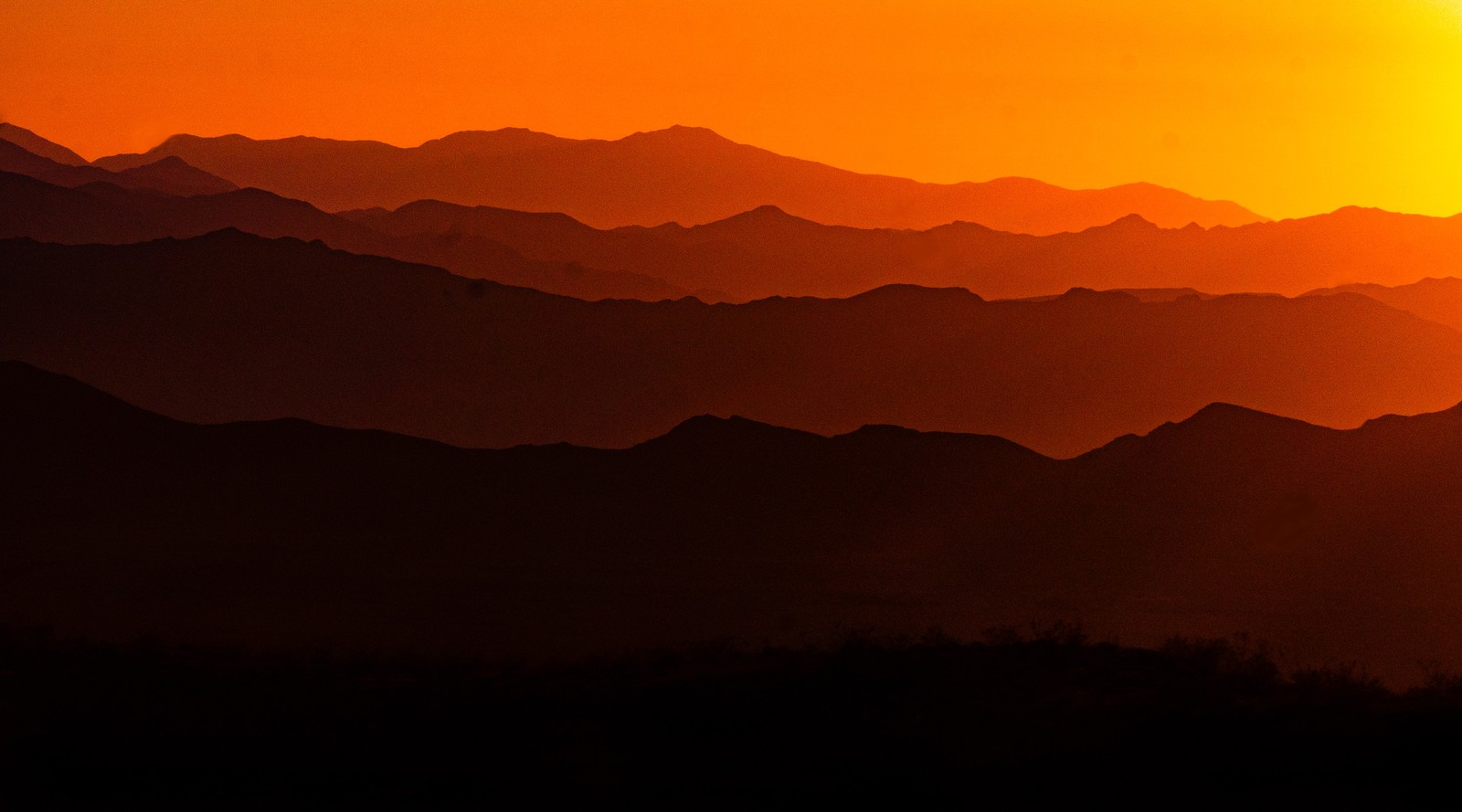 Arafed view of a mountain range at sunset with the sun setting (mountain, sunset, silhouette, cloud, atmosphere)