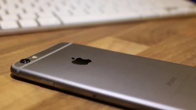 Sleek Apple Smartphone on Wooden Surface with Keyboard in Background