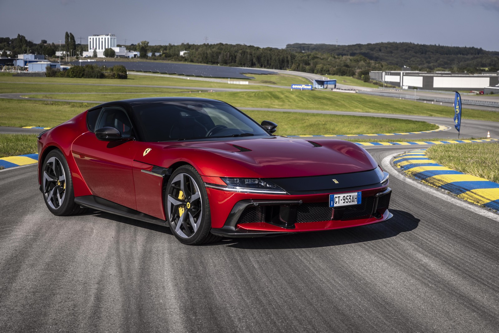 Un coche deportivo rojo conduciendo en una pista con un campo verde al fondo. (ferrari 12 cilindros, pista de carreras, 5k, 8k, coches deportivos)