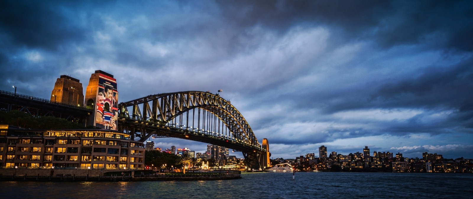 Uma vista de uma ponte sobre um corpo de água com uma cidade ao fundo (ponte da baía de sydney, ópera de sydney, sydney opera house, ponte, marco)