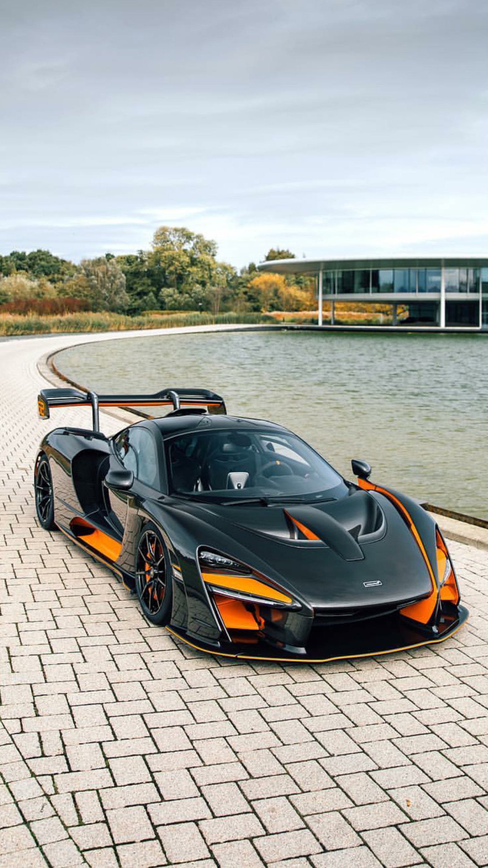 Un primer plano de un auto deportivo negro y naranja estacionado en una carretera de ladrillos (mclaren, senna, nuevo, coche, hipercoche)