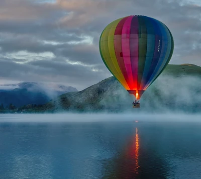 Montgolfière colorée au-dessus d'un lac brumeux et des collines au crépuscule