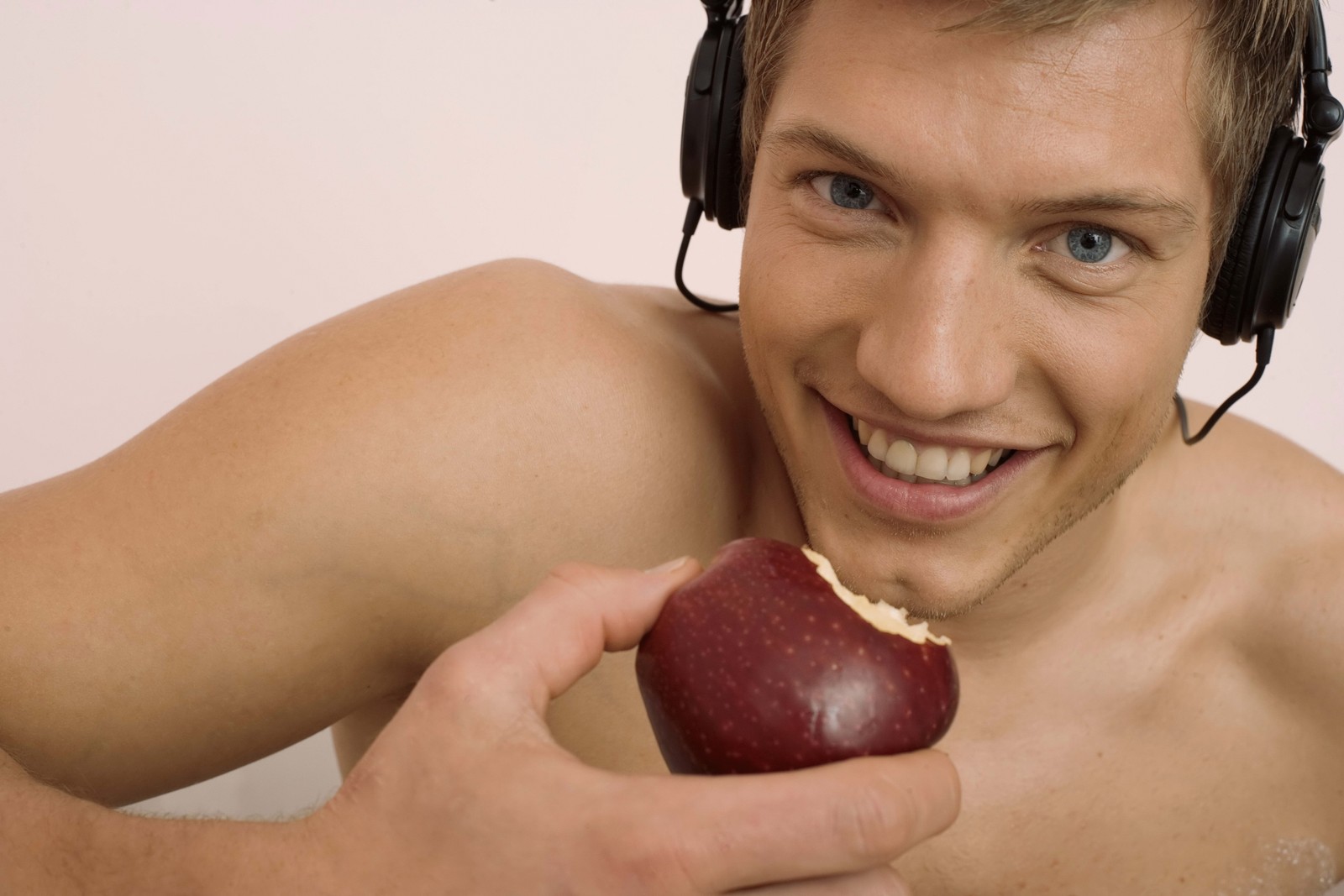 Um homem com fones de ouvido comendo uma maçã (comida, fone de ouvido, músculo, boca, pescoço)