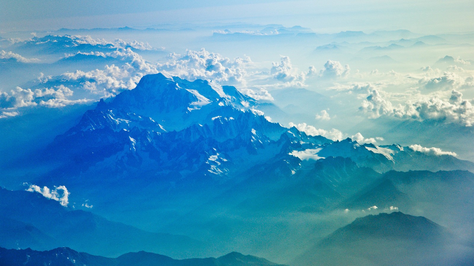 Mountains are seen from an airplane window as the sun shines (mountains, clouds, nature, scenery, landscape)