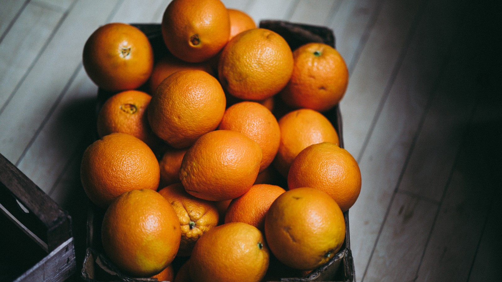 Es gibt viele orangen in einem korb auf dem boden. (orange, frucht, mandarine, clementine, zitrusfrüchte)