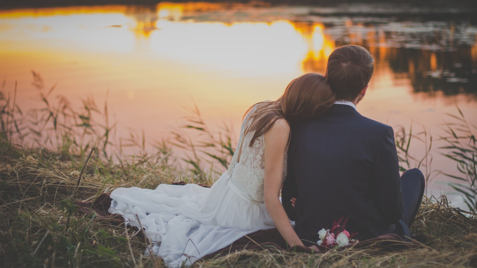 Un hombre y una mujer sentados en el suelo cerca de un lago (romance, belleza, amor, luz solar, vestido)