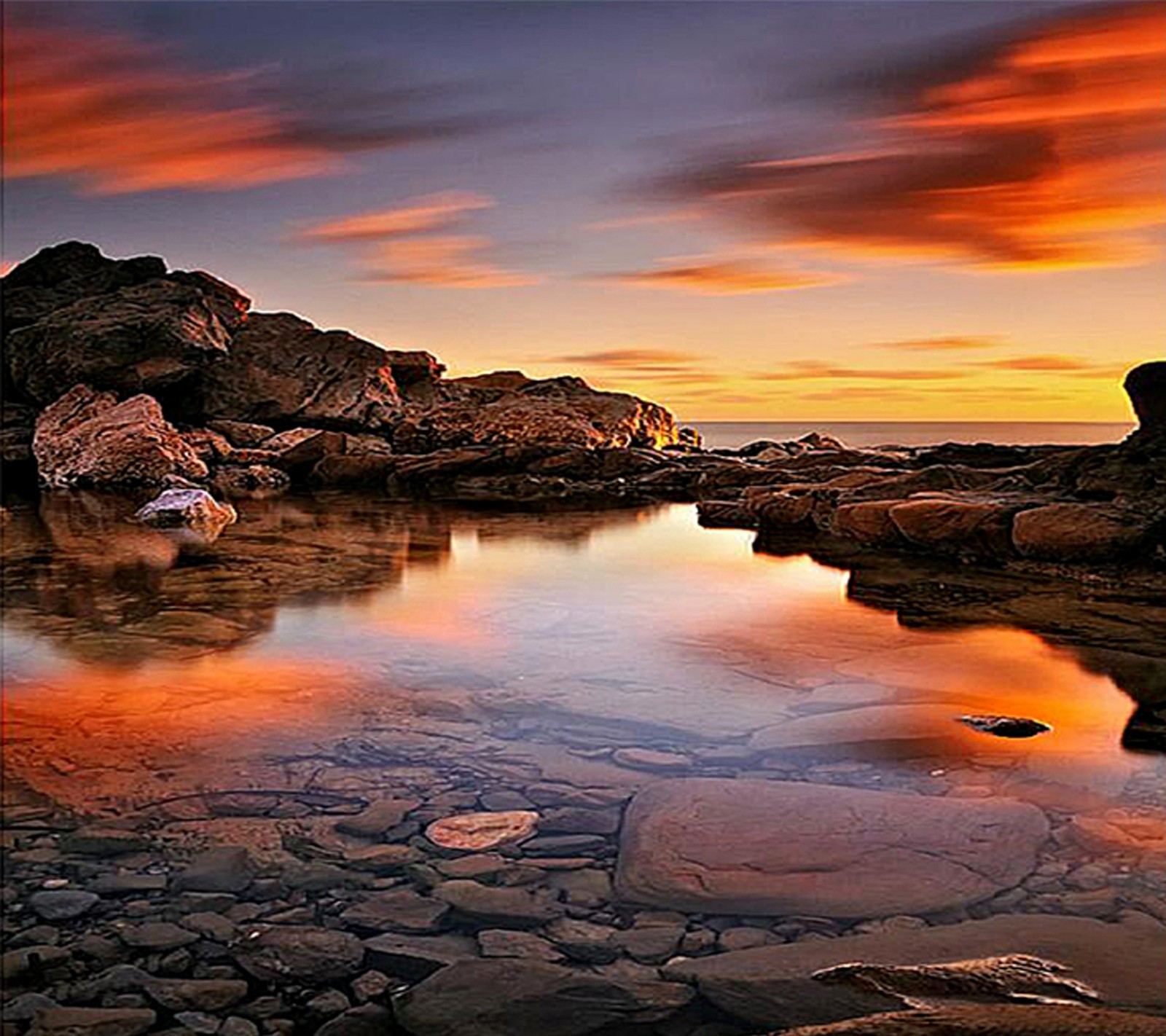 Sunset over a rocky beach with a body of water and rocks (nature, wallpaper)