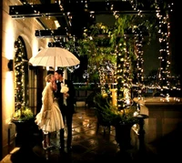 A romantic couple sharing a kiss under an umbrella, surrounded by twinkling lights.