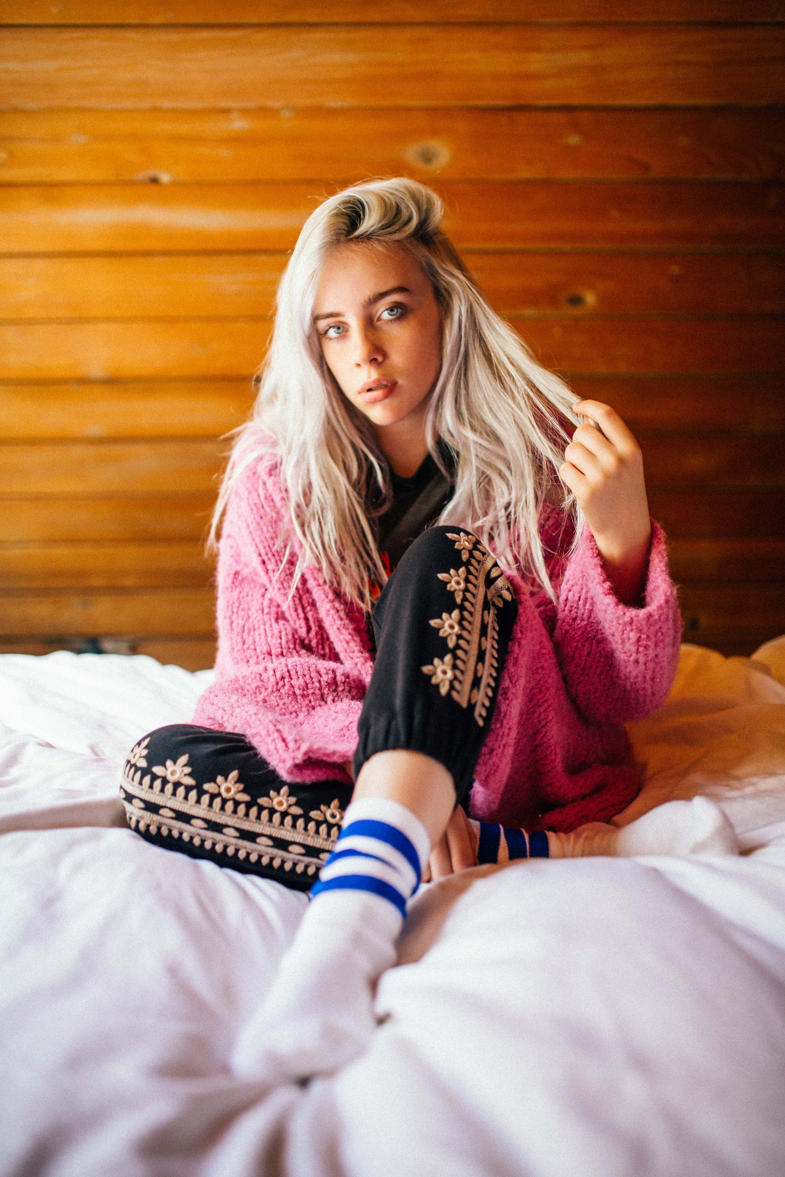 Mujer rubia sentada en la cama con un suéter rosa y leggins negros (chico malo, hermoso, billie eilish, chica, niña)