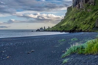 Ruhiger schwarzer Sandstrand gegen azurblaues Wasser und dramatische Klippen