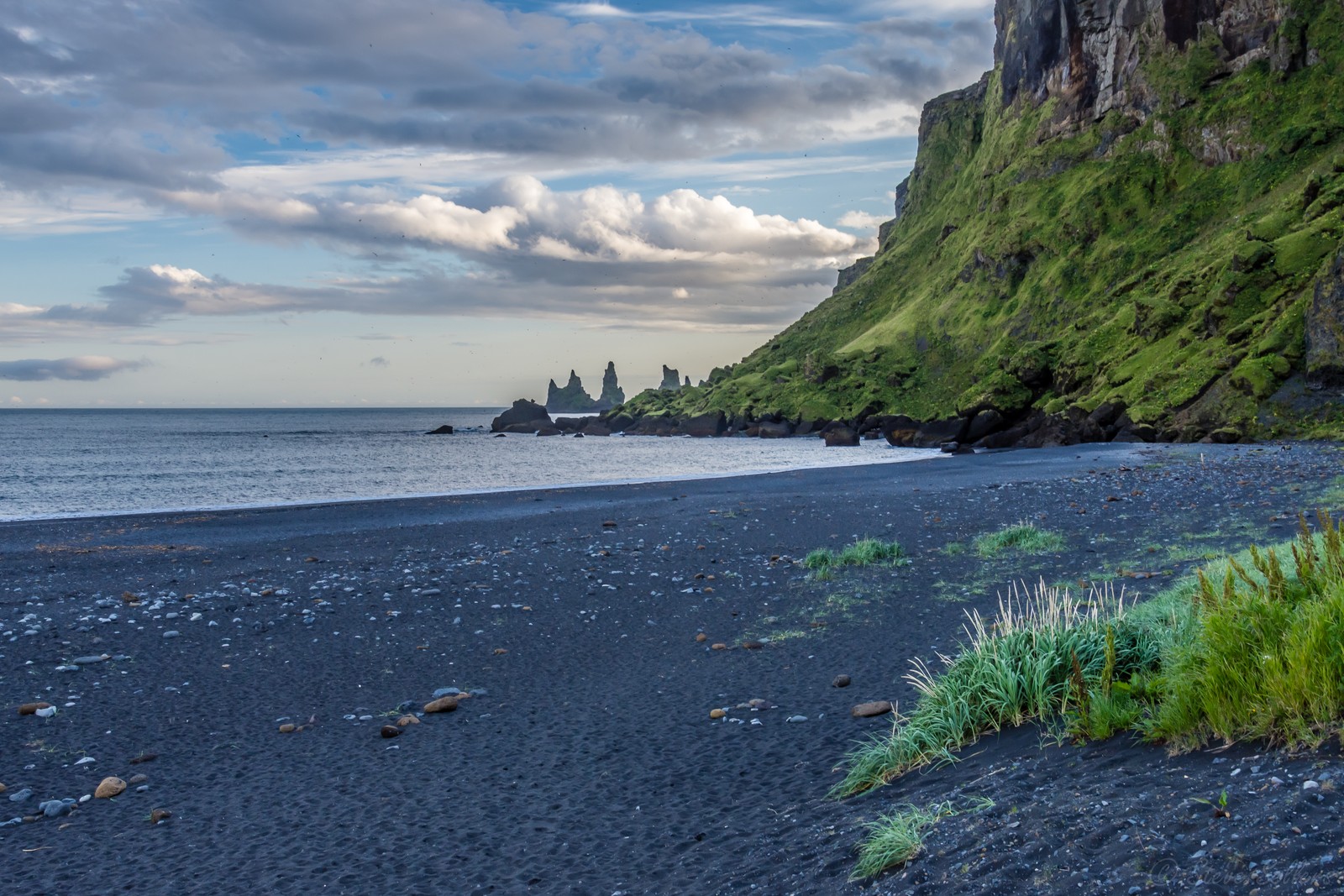 Uma praia de areia preta com uma montanha verde ao fundo (nuvem, água, recursos hídricos, montanha, paisagem natural)