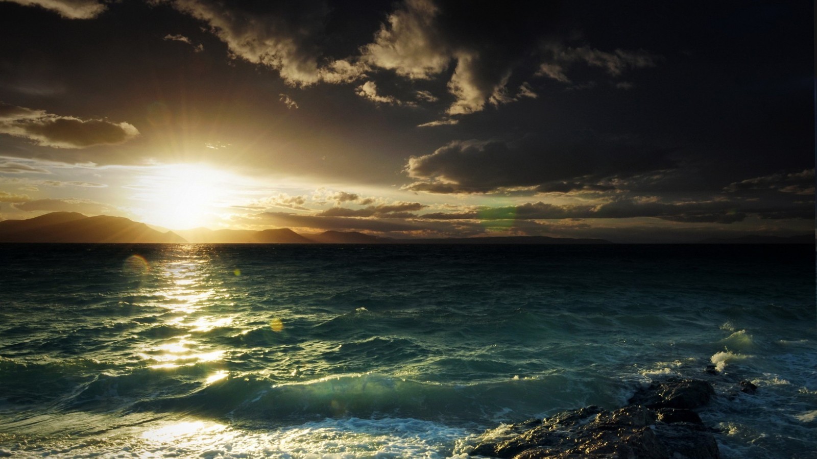 A view of the sun setting over the ocean with rocks in the foreground (coast, shore, sea, ocean, horizon)