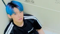 Yeonjun from TXT with blue hair in a contemplative pose against a graffiti-covered wall.