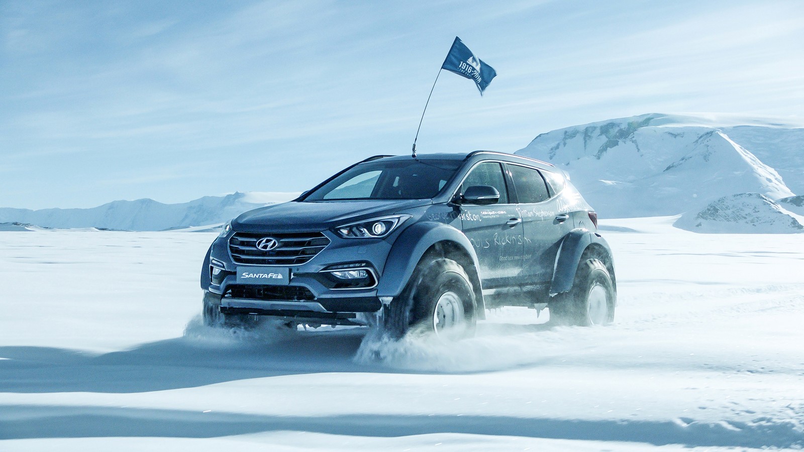 Um suv azul dirigindo pela neve com uma bandeira em cima. (polo sul, carros, condução, hyundai, tração nas quatro rodas)