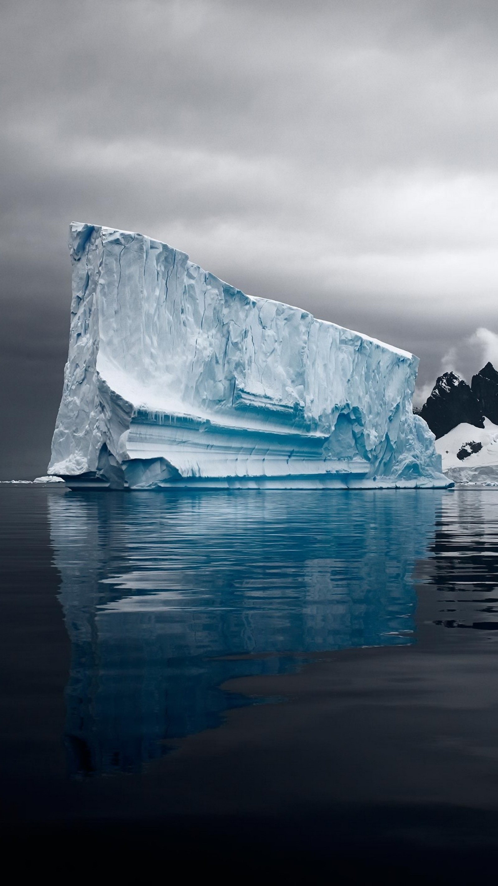 Um grande iceberg flutuando na água com uma montanha ao fundo (iceberg, calota polar, antártica, antarctica, oceano ártico)