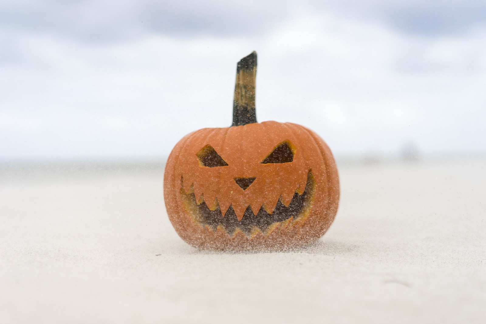 Es gibt einen kleinen kürbis mit einem geschnitzten gesicht am strand. (halloween, oktober, beängstigend, gruselig)