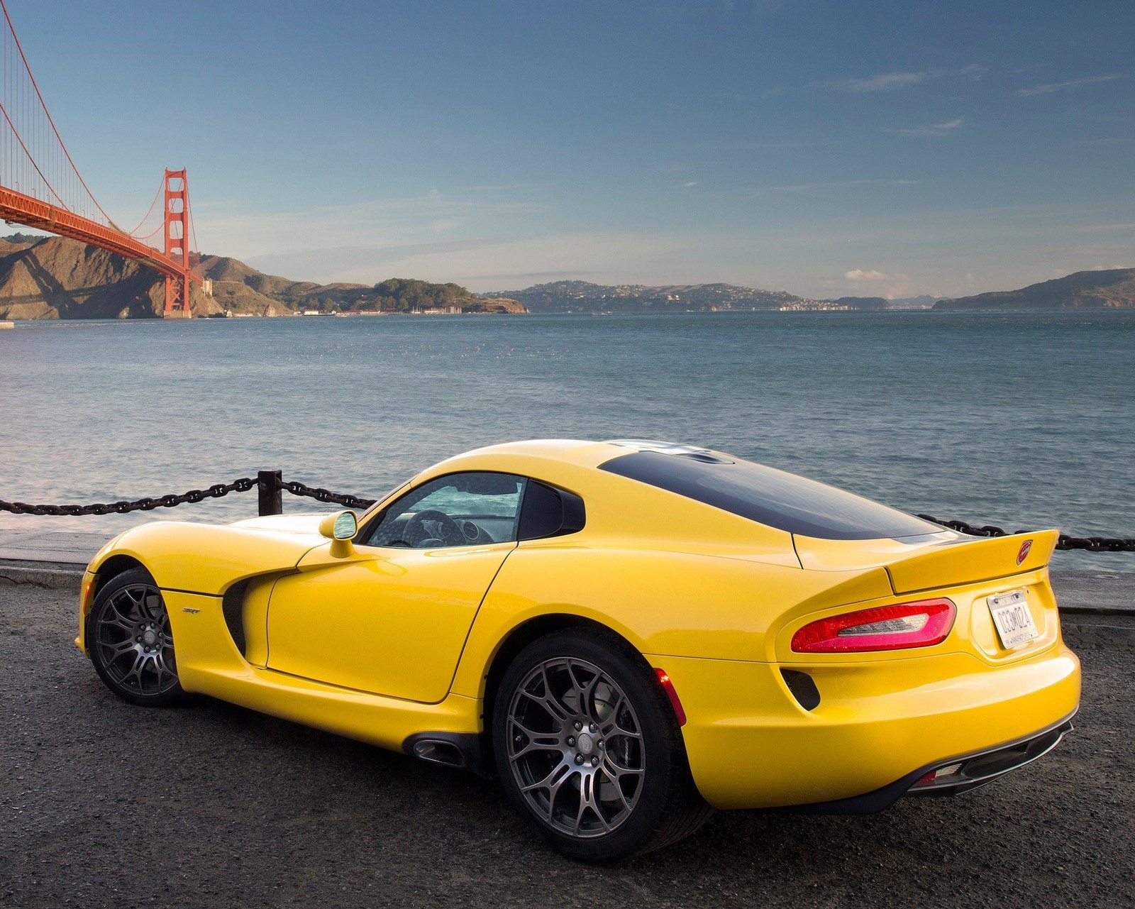 Yellow sports car parked near the golden gate bridge in front of the water (bridge, car, dodge, ocean, viper)