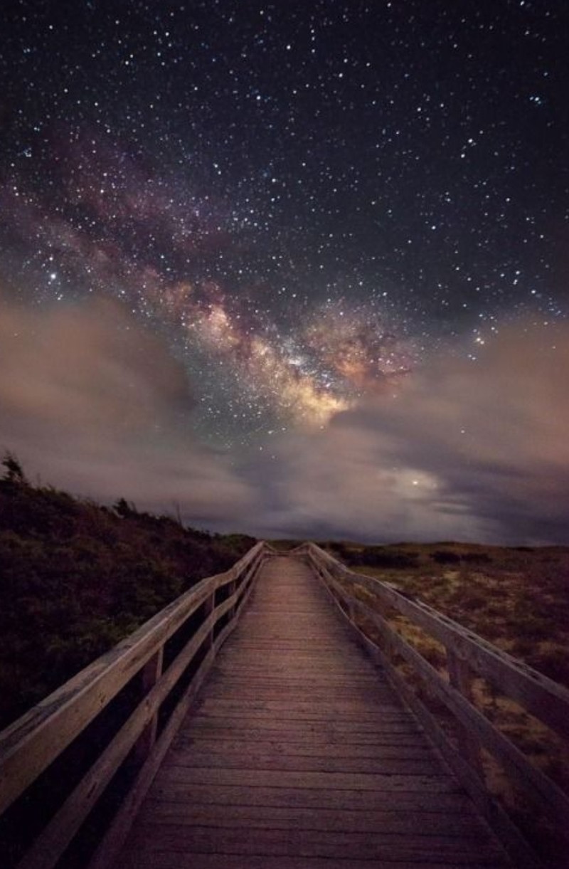 Un camino de madera que lleva a una playa con un cielo lleno de estrellas (playa, noche, estrellas, caminar)