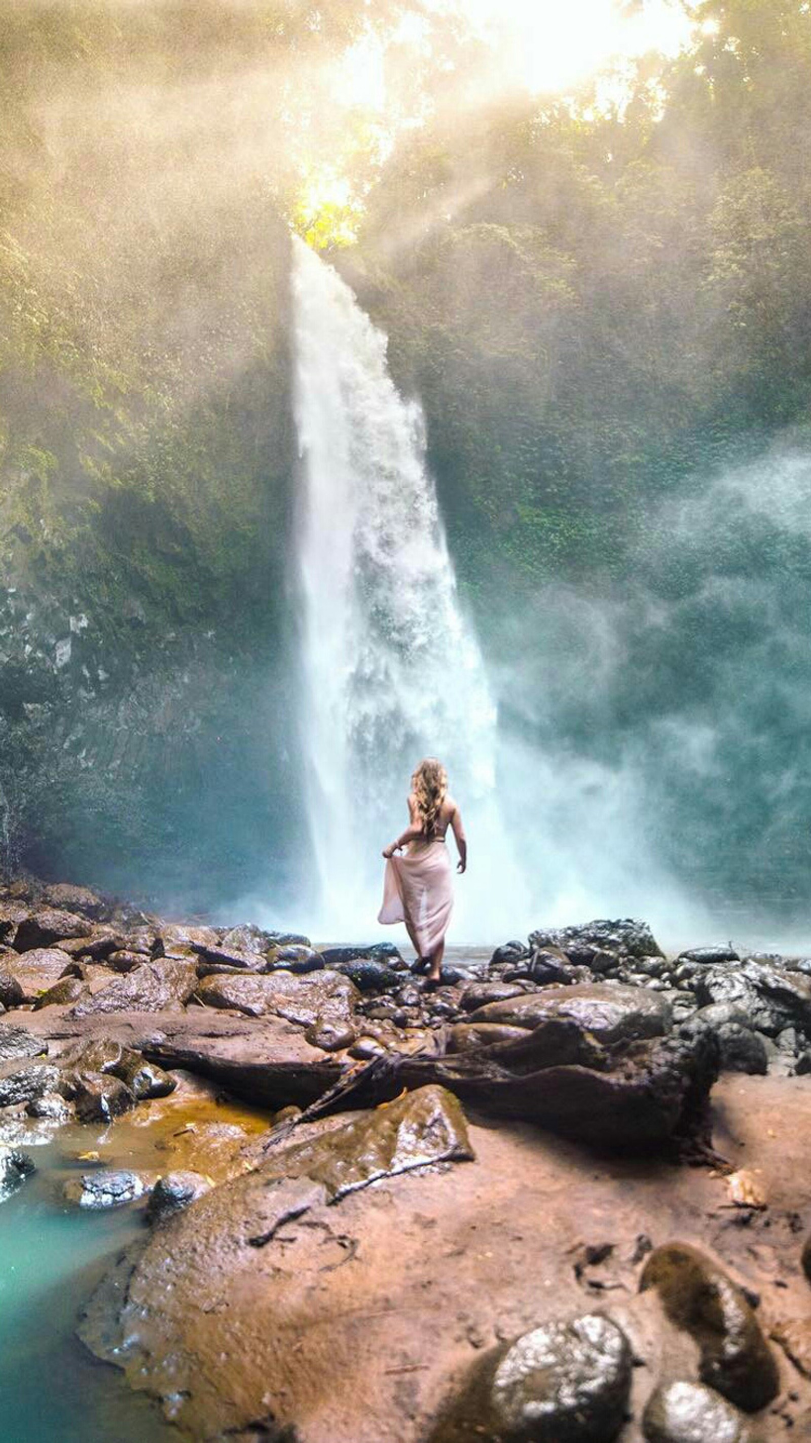 There is a woman standing on a rock near a waterfall (girl, nature, people, waterfall)