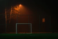 Campo de fútbol iluminado por la noche con portería y niebla envolvente