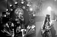 Guns N' Roses se produisant en direct lors de la "Not in This Lifetime Tour", avec Axl Rose et Slash dans un cadre dramatique en noir et blanc.