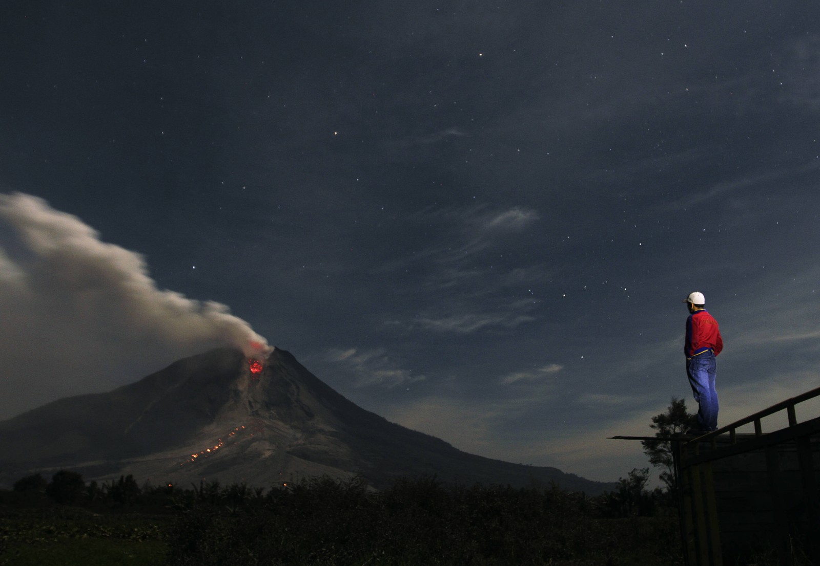 Un volcan avec un homme debout sur un rebord regardant le ciel (mont sinabung, mount sinabung, volcan, nuit, nuage)