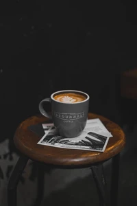 Café cortado com arte de latte servido em uma caneca estilosa em um banco de madeira rústica, complementado por cartões postais vintage.