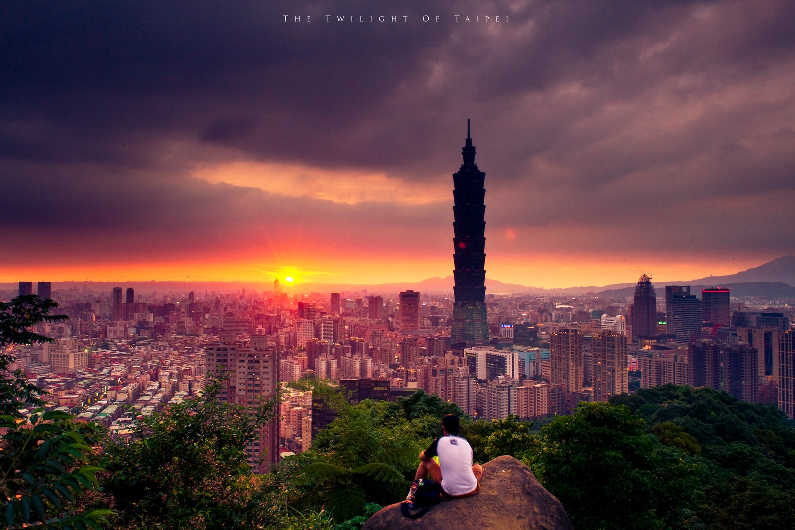 Arafed view of a man sitting on a ledge overlooking a city (taipei 101, city, cityscape, landmark, urban area)