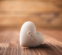 Heart-shaped white stone with the word "LOVE" engraved, set against a warm, wooden background.