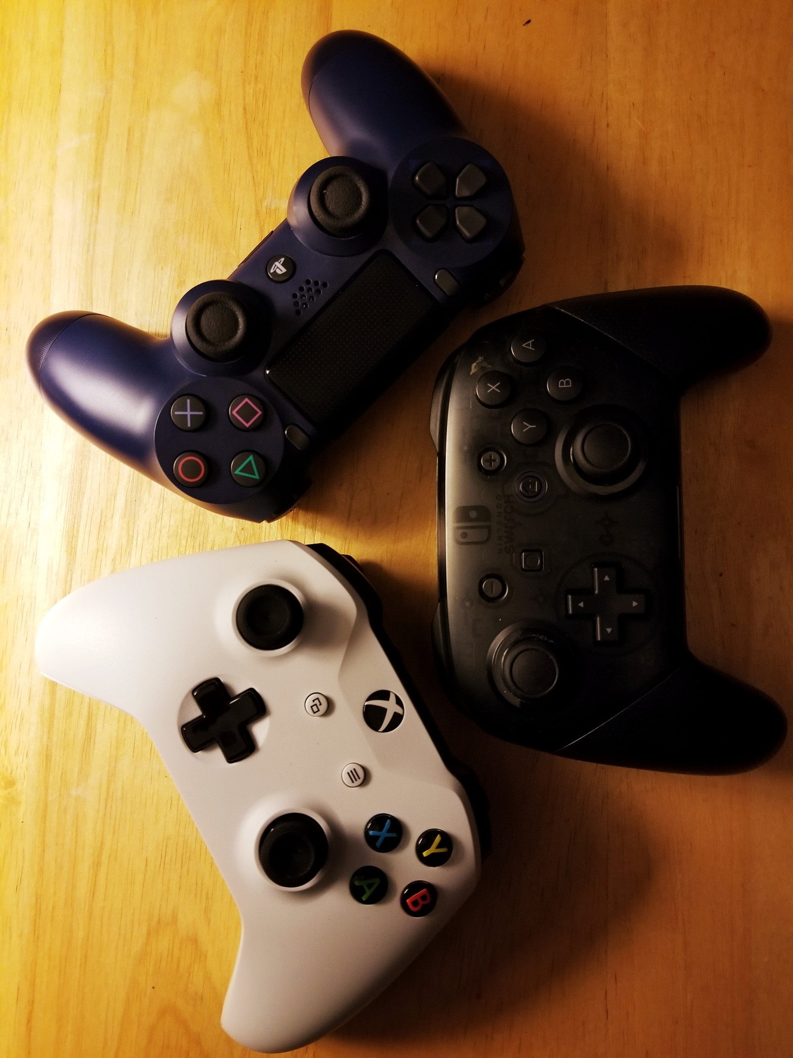 Two controllers are sitting on a table next to each other (controller, playstation, xbox, nintendo switch)