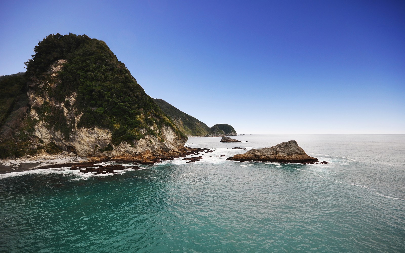 Uma vista de uma costa rochosa com um corpo d'água (linha costeira, paisagem marinha, paisagem, horizonte, montanhas)