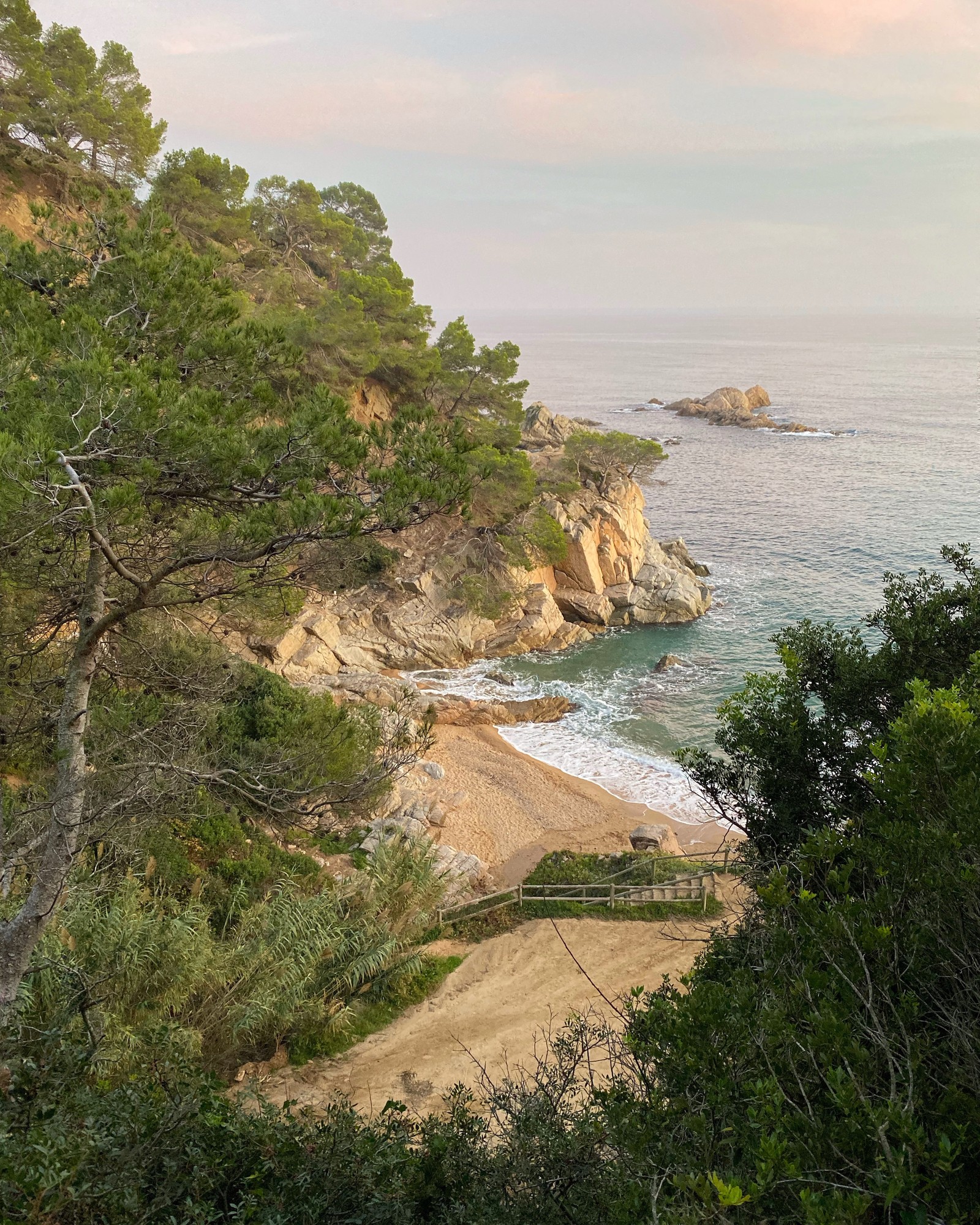 There is a view of a beach from a hill with a bench (coast, promontory, headland, natural landscape, shore)