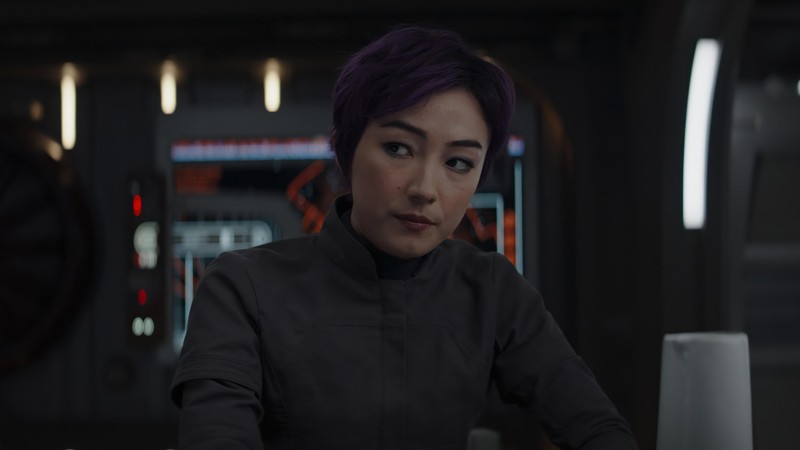 Женщина с фиолетовыми волосами сидит за столом в комнате (сабина рен, sabine wren, сериал ахсока, ahsoka series, дисней)