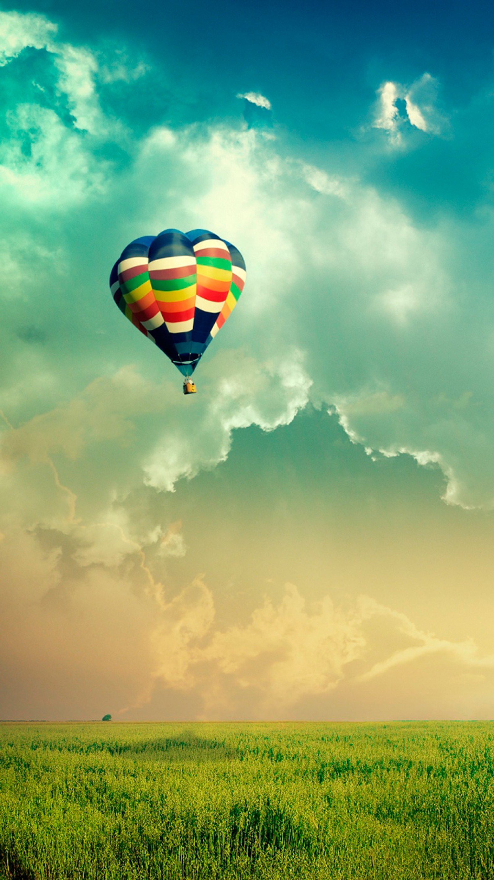 There is a colorful hot air balloon flying over a field (balloon in sky, colors, nature)