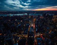 Uma vista aérea de tirar o fôlego do horizonte de uma cidade ao pôr do sol, ruas iluminadas e um rio tranquilo refletindo os tons vibrantes do céu.