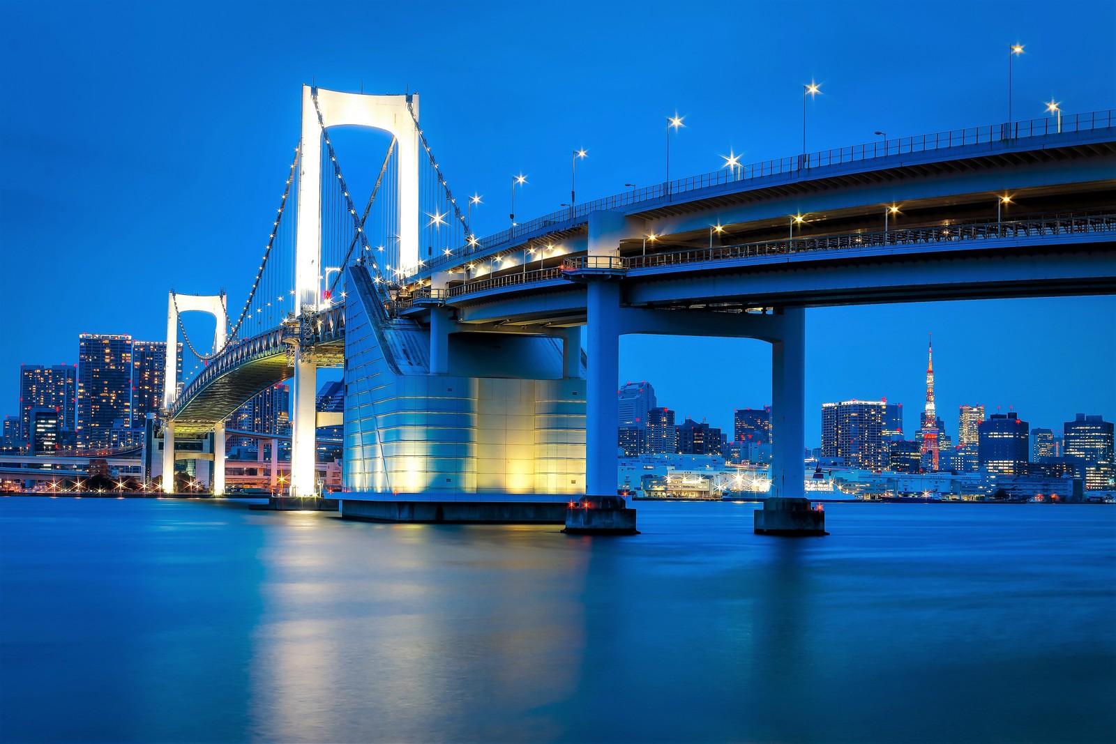 Vista de un puente sobre un cuerpo de agua con una ciudad al fondo (puente arcoíris, puente colgante, puente, hito, ciudad)