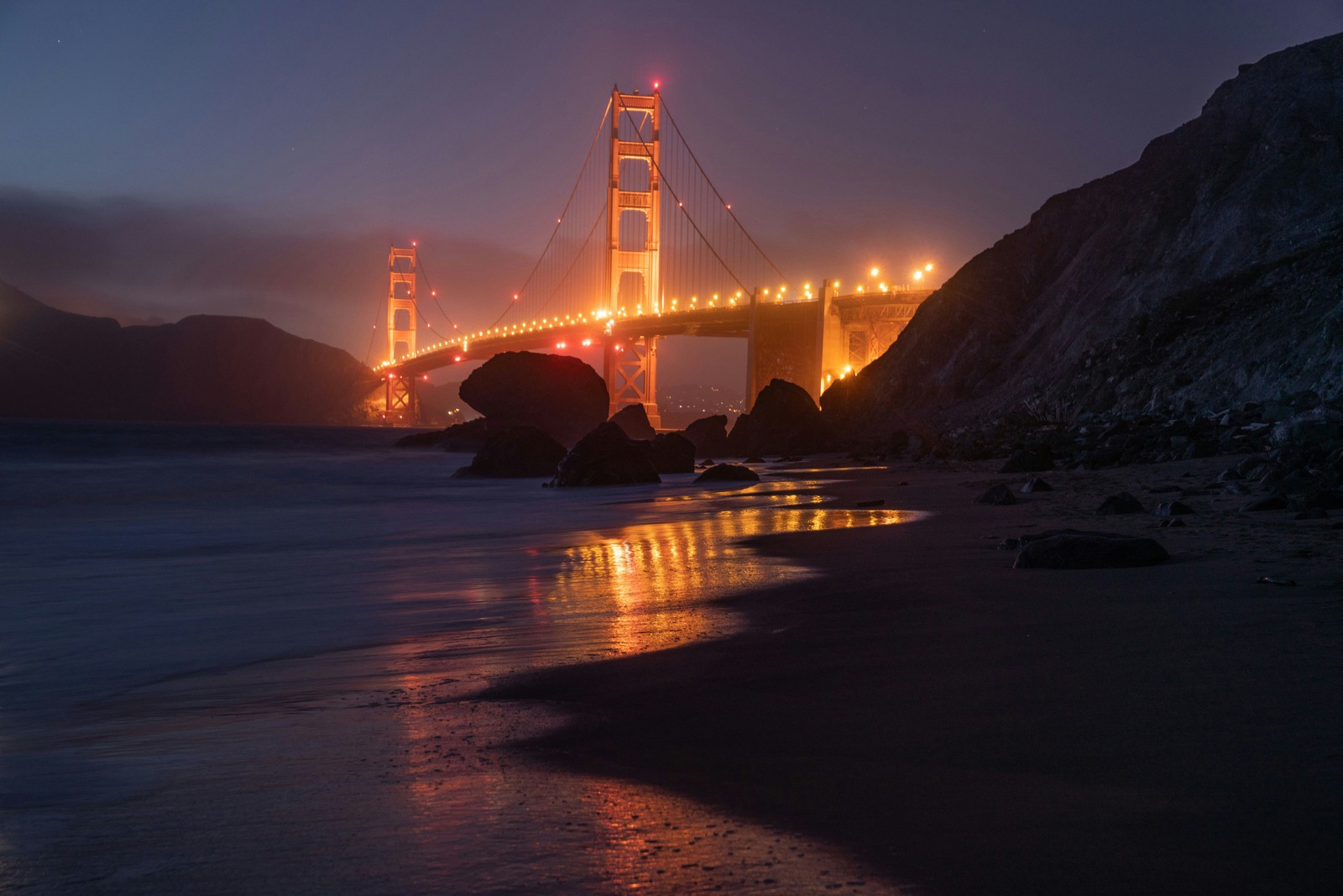 Una vista aérea de un puente sobre un cuerpo de agua por la noche (puente golden gate, golden gate bridge, iluminado, noche, reflexión)