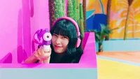 Momo de TWICE Apuntando Juguetonamente con una Pistola de Agua en un Entorno Colorido