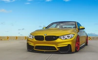 Stunning yellow BMW M4 with striking red wheels, showcasing a sleek and aggressive design against a clear blue sky.