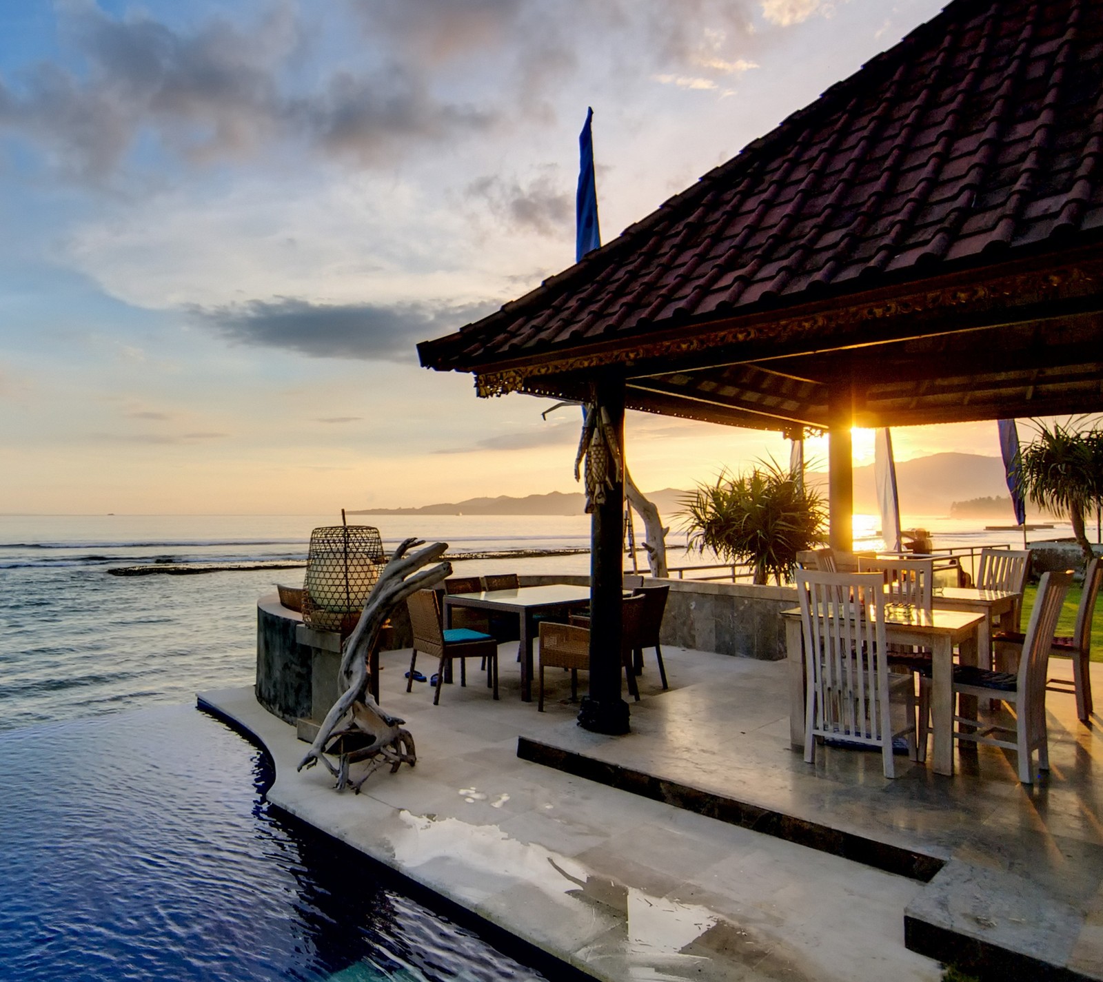 Há uma grande piscina com uma mesa e cadeiras ao lado. (casa, piscina, mar, por do sol)