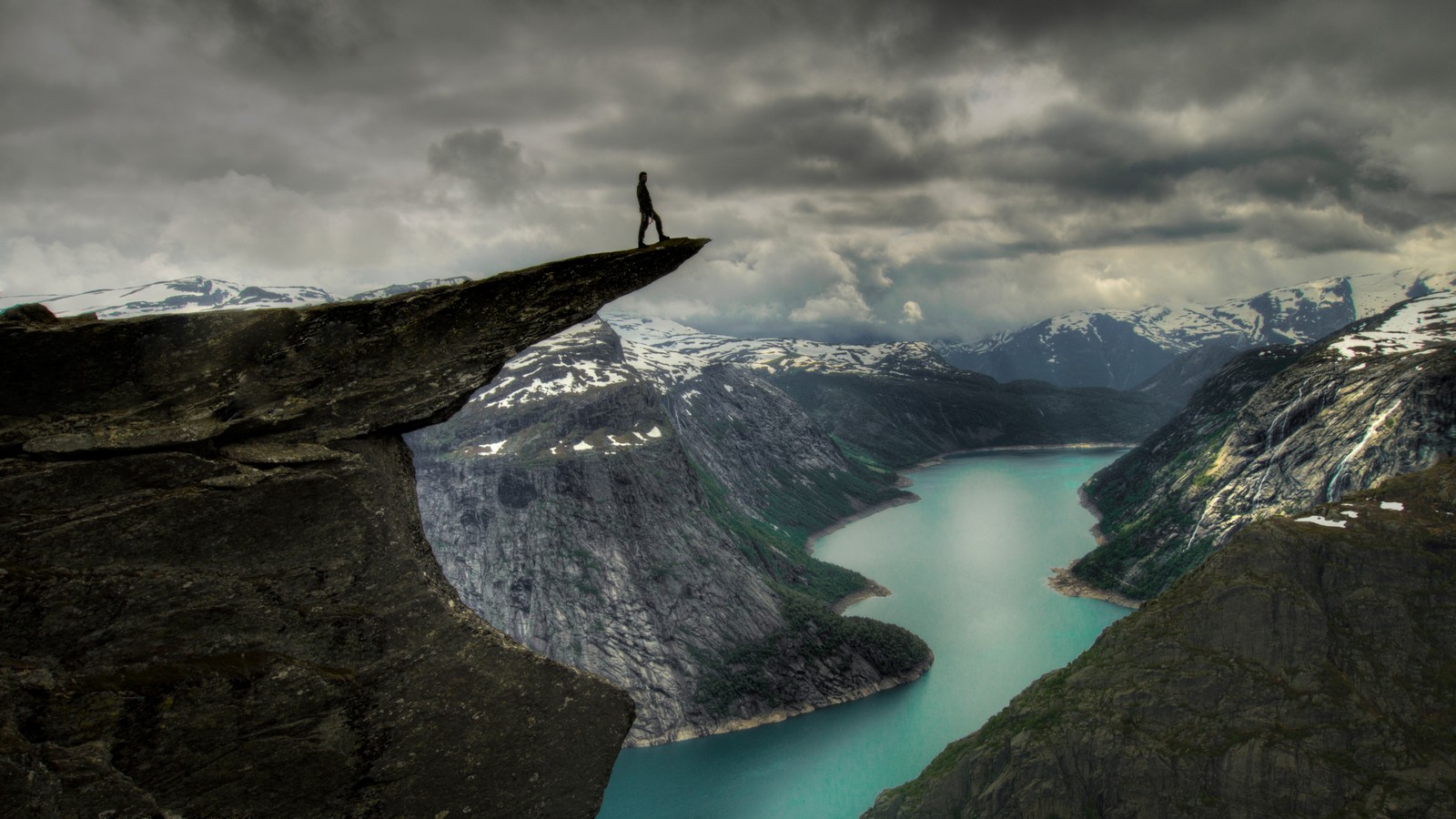 Arafed view of a person standing on a cliff overlooking a lake (trolltunga, fjord, bergen, tourist attraction, cliff)