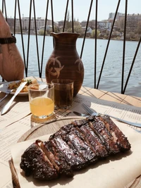 Bife de carne grelhado com bebidas refrescantes à beira do lago