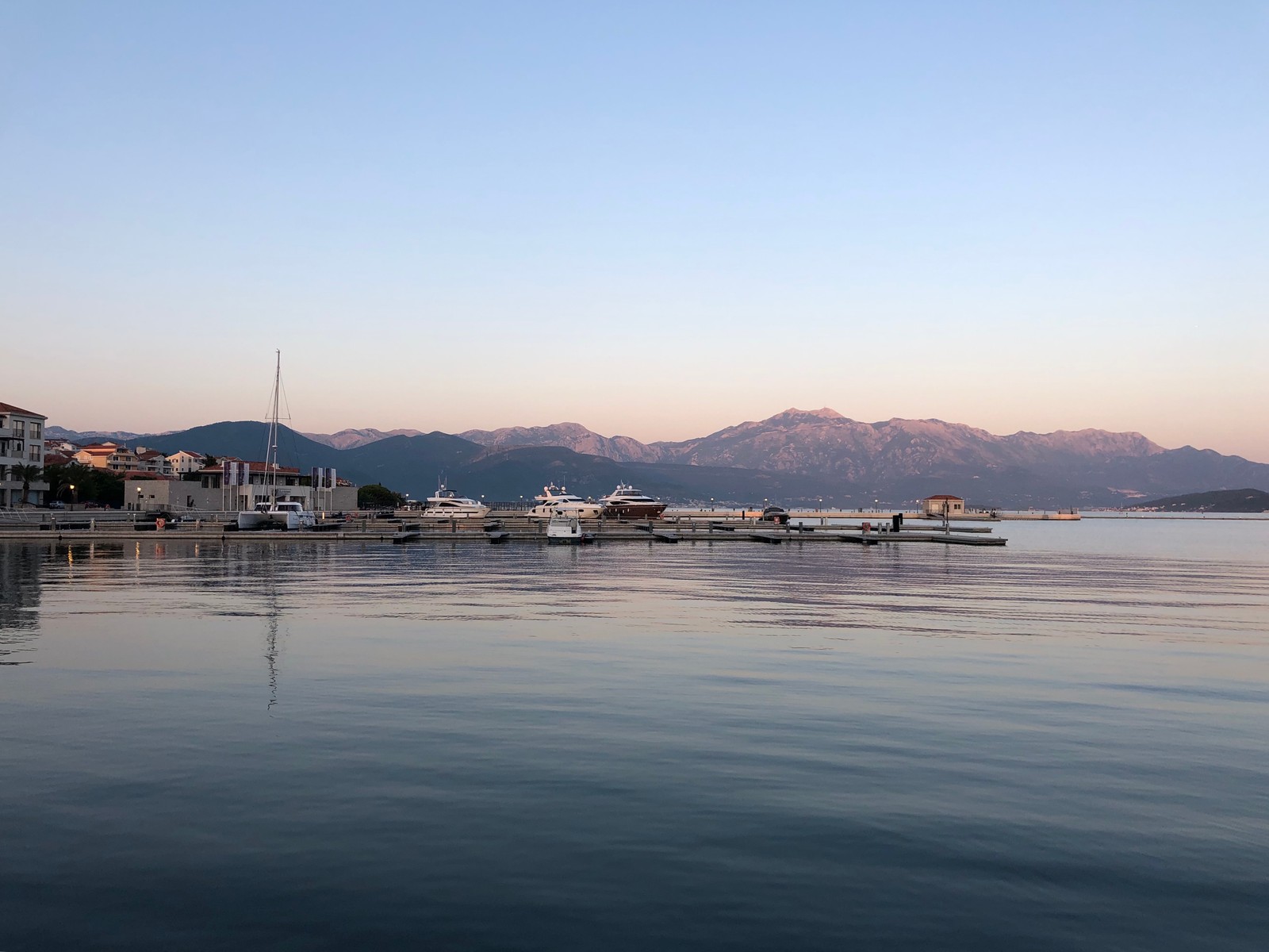 Boats are docked in the water near a city on a clear day (mountainous landforms, liquid, water resources, water, mountain range)