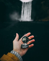 Explorando a natureza: uma mão segurando uma bússola contra uma majestosa cachoeira