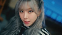 Chaeyoung de TWICE con llamativos cabellos plateados, mirada cautivadora y un elegante atuendo a rayas.