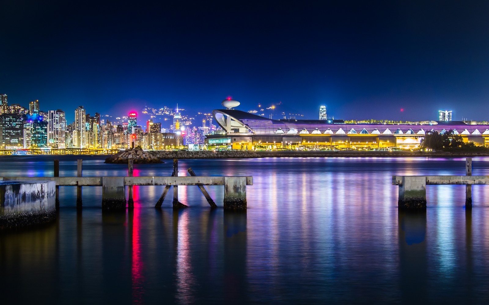 Вид на городской пейзаж ночью с пирсом и лодкой (kwun tong ferry pier, гонконг, hong kong, гавань виктория, kai tak cruise terminal)